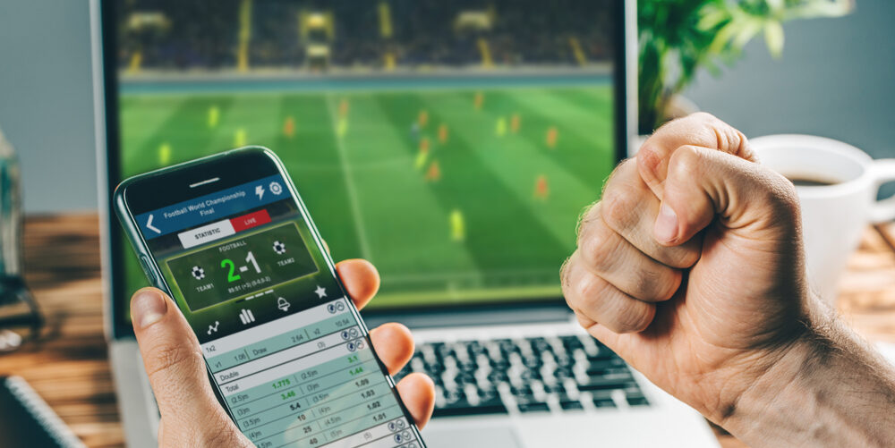 Un hombre que gana en las apuestas de fútbol en línea mientras mira fútbol en una computadora portátil y revisa el teléfono inteligente