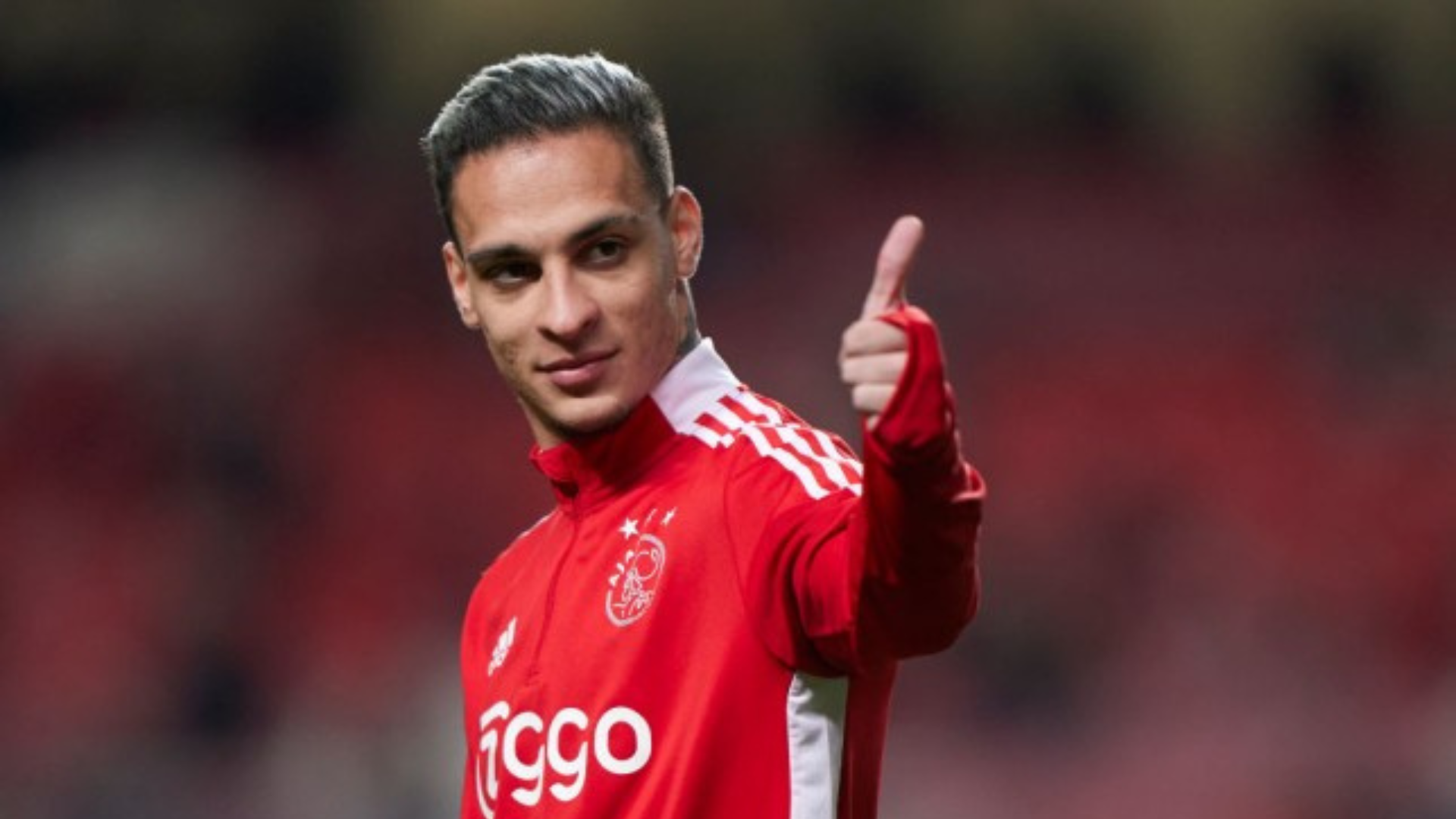 Ajax Winger Antony wearing red and white jacket and doing thumbs up hand gesture