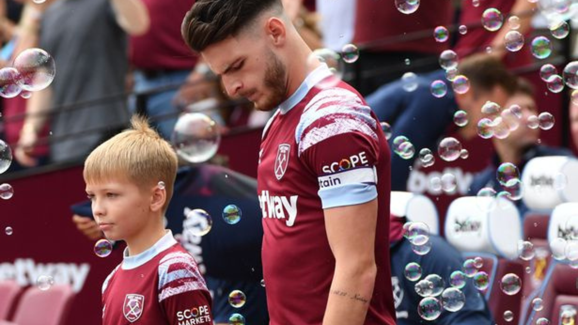 Declan Rice standing showing his tattoo on his arm with some bubbles around him