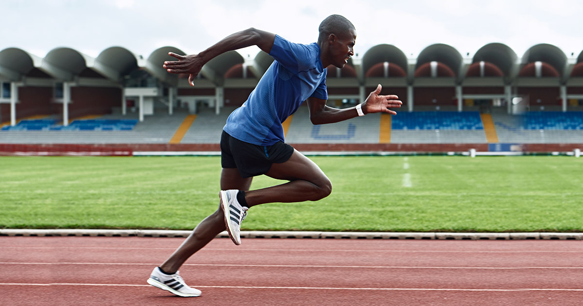 A man wearing a blue t-shirt and a black short with a white shoe running on a track