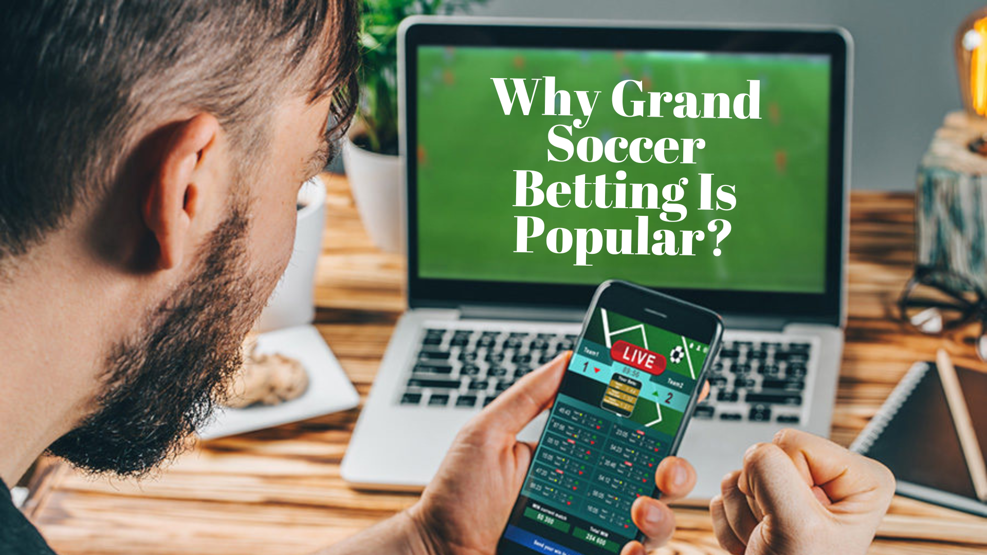 A man holding a phone while in front of the laptop with words Why Grand Soccer Betting Is Popular?