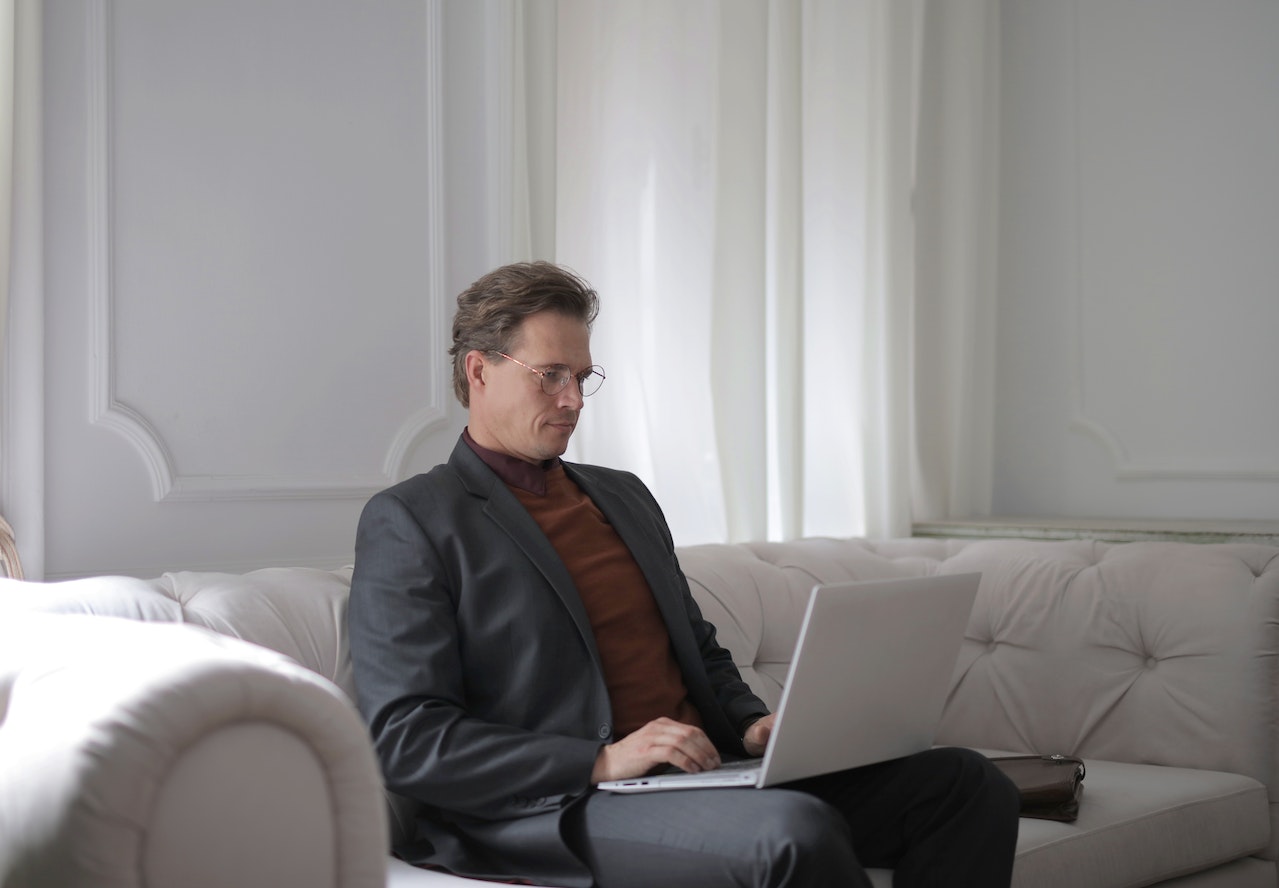 A Man With Glasses Sitting on a White Couch Using Laptop