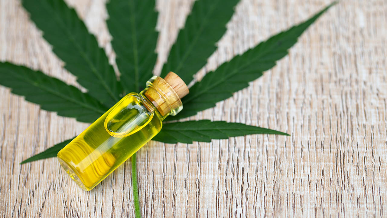 A closed transparent bottle filled with CBD oil laying on a cannabis leaf
