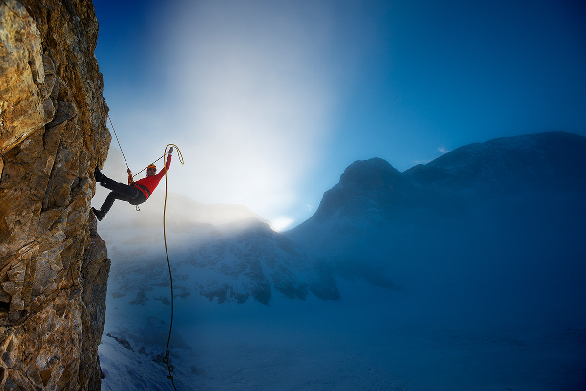 A man wearing a red jacket climbs a snow-covered mountain without a snow-covered hillside as the sun sets. And the bluish nature is visible