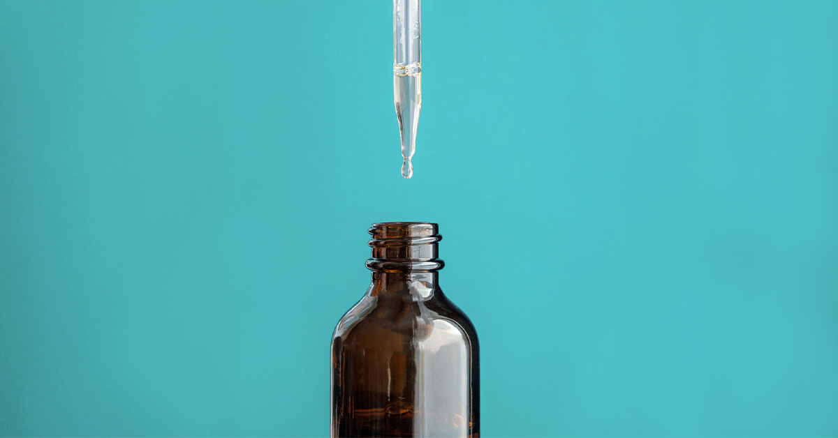 A droper dropping CBD oil into an opened bown bottle