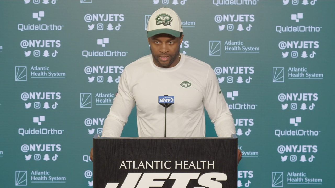 Randall Cobb wearing a white long sweater and white cap on a podium