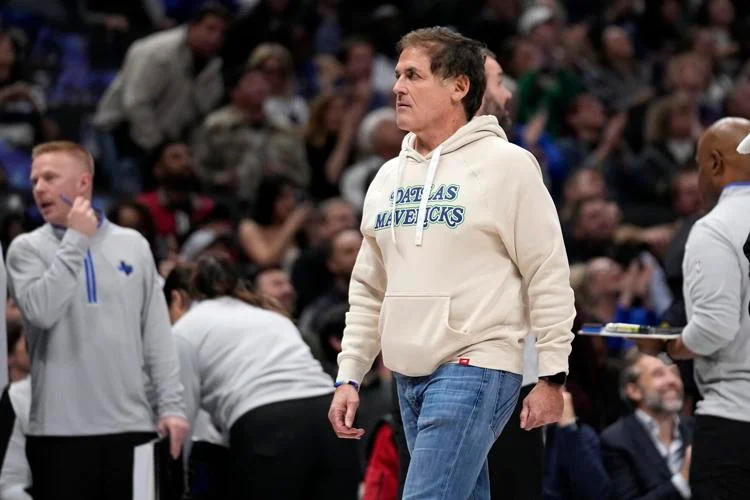 Mark Cuban is walking while people are sitting.