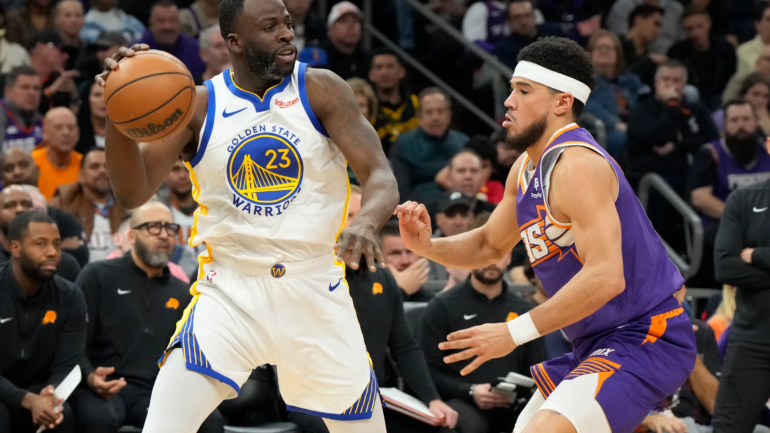 Golden State Warriors forward Draymond Green (23) shields the ball from Phoenix Suns guard Devin Booker during the first half of an NBA basketball game, Tuesday, Dec. 12, 2023, in Phoenix.